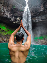 Rear view of shirtless man looking at waterfall