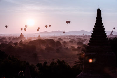 Hot air balloons flying over temples against sky during sunset