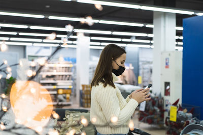 Woman wearing face mask and protective gloves in store uses phone. today people lifestyle concept