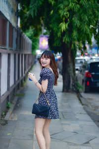 Portrait of young woman standing on footpath