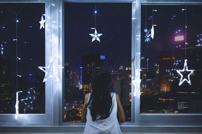 Rear view of girl looking through window at home