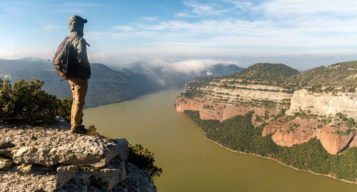 Rear view of man standing on rock against sky