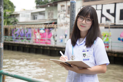 Portrait of female doctor holding book while standing outdoors