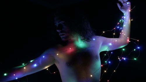 Side view of woman with arms raised standing against black background