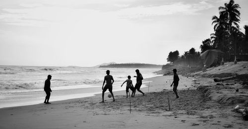 Silhouette friends playing soccer at beach