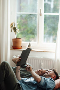 Cheerful couple with digital tablet lying on bed at home