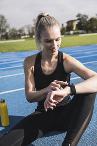 Young sportswoman using smart watch on track