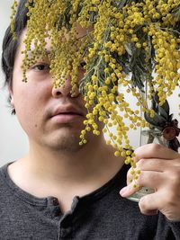 Portrait of young man holding golden wattle flowers in vintage vase.