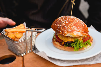 Cropped image of person eating french fries and burger at restaurant