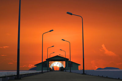 Street lights and built structure against orange sky at sunset