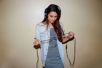 Young woman listening to music against wall