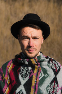 Close-up portrait of a man posing in rural area in a poncho and hat