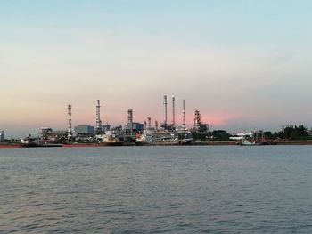 Sea by factory against sky during sunset