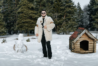 Portrait of young man wearing warm clothing while standing on snow covered field