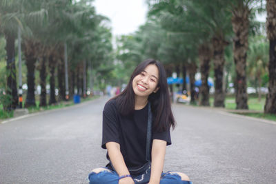 Portrait of smiling woman sitting on road against trees