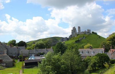Cottage buildings and castle ruins on hill against cloudy sky