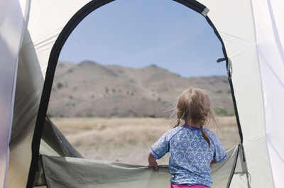 Rear view of girl looking at mountain while standing in tent