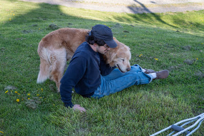 Golden retriever dog cuddles with a man sitting on grass with crutches