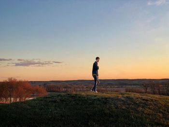 Portrait of boy walking on field against sky during sunset