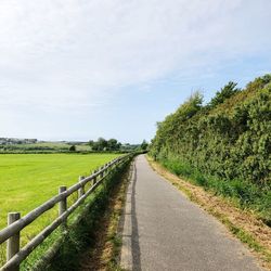 Empty road amidst field against sky