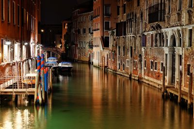 Boats moored in canal amidst buildings in city at night