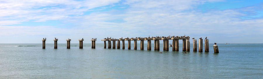 Wooden posts on pier over sea against sky