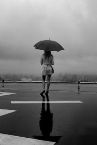 Woman with umbrella walking on wet shore against sky