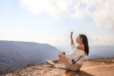Woman sitting on top of mountain range against sky