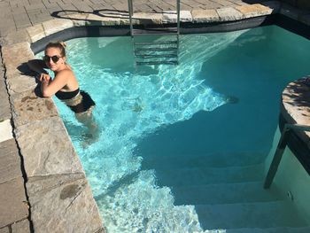 High angle portrait of young woman wearing sunglasses standing in pool