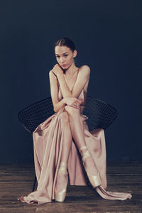 Portrait of a ballerina in a pink dress is sitting on a chair with her leg in the slit of the dress