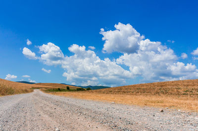 Dirt road amidst landscape against blue sky