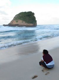 Woman crouching at beach against sky