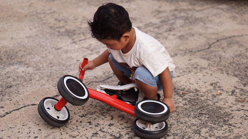 Cute baby boy crouching by cycle on land