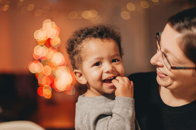 Close-up of mother with cute son against illuminated christmas lights at home