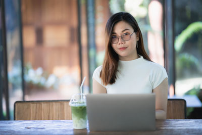 Portrait of young woman using phone while sitting on table