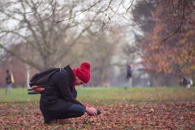 Side view of man crouching while holding camera at field