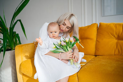 Mother with child in white clothes on a yellow sofa bouquet of flowers tulips spring