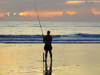 Rear view of silhouette man on beach during sunset