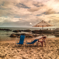 Deck chairs on beach against sky during sunset