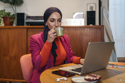 Young woman using laptop while sitting on table