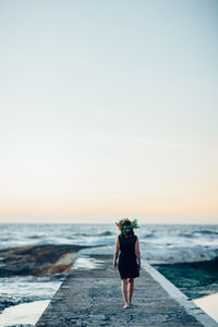 Rear view of woman walking on beach against clear sky