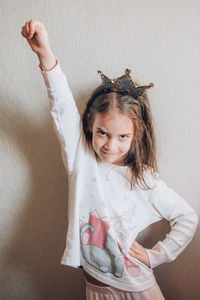 Portrait of young woman with arms raised standing against wall