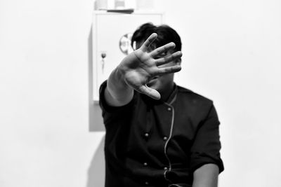 Man covering face with hand while standing against wall