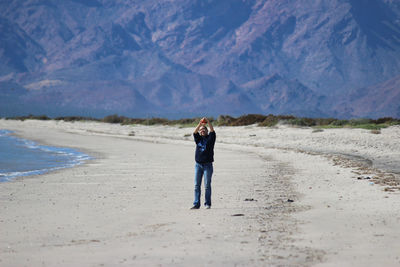 Woman flying kite standing at shore of beach