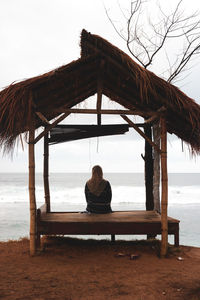 Rear view of woman sitting on pier at beach against sky