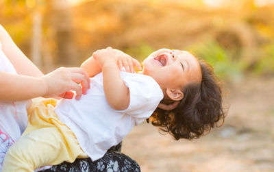 Midsection of mother tickling toddler daughter while sitting outdoors