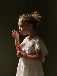 Cute girl blowing bubble against black background