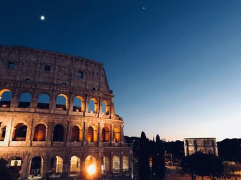 Low angle view of illuminated coliseum against blue sky at night