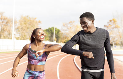 Male and female athlete doing elbow bump while walking on track during sunny day