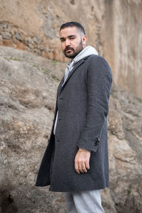 Caucasian man standing on a rock outdoors wearing grey winter coat